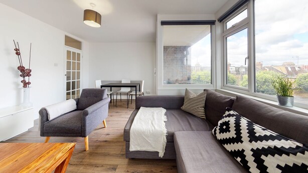Een moderne woonkamer met een grijze bank, een houten salontafel en een eethoek met een witte tafel en stoelen.
