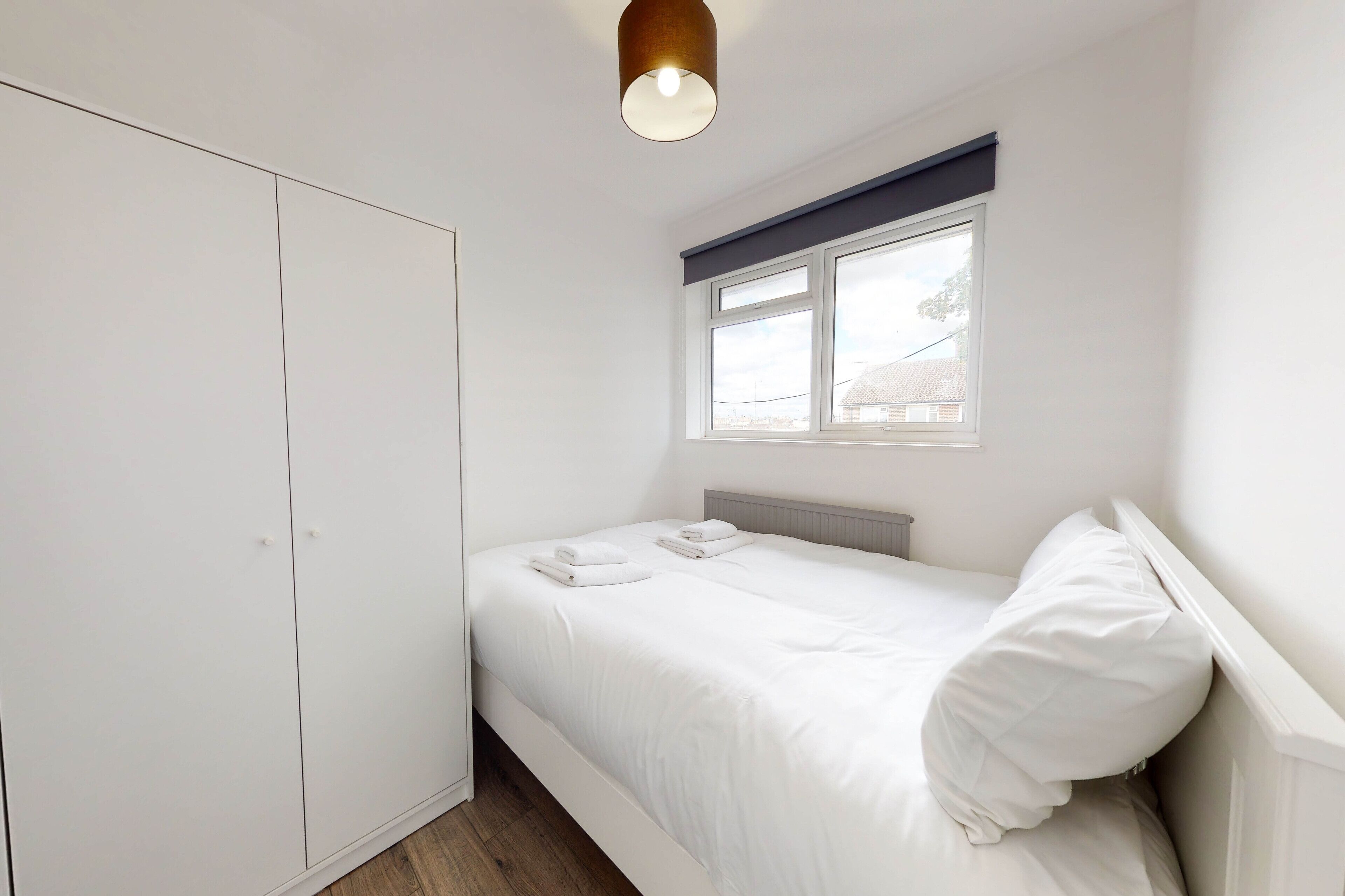 Un dormitorio con una cama individual, ropa de cama blanca, un armario, una ventana con vistas y una lámpara de techo.