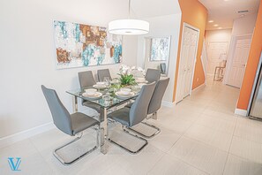 A modern dining area with a glass table, grey chairs, and white plates. - Kids-Friendly, Family-Friendly 3BD Deluxe Townhome 1603 (Clermont)