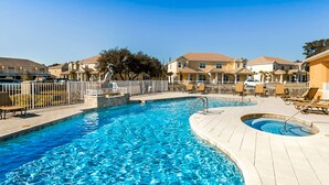 Une piscine avec un plongeoir, entourée d’une clôture et située à côté d’une rangée de maisons.