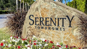 Une pancarte en pierre sur laquelle est inscrit « Serenity Townhomes », entourée d’herbe et de fleurs.