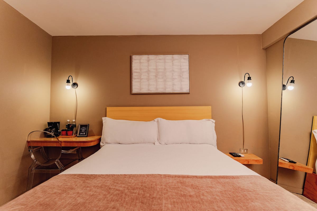 A hotel room with a bed, bedside tables, a desk with a chair, a mirror, and two wall-mounted lamps.