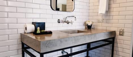 Une salle de bain avec un mur en briques blanches, un grand miroir, un lavabo avec un porte-serviettes et une chaise verte.