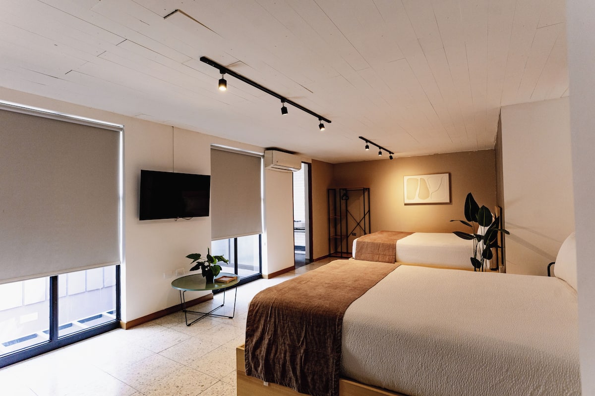 A modern hotel room with a large bed, a TV, a small table with a plant, and a window with a view.