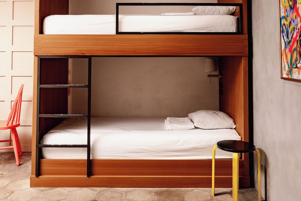 A bunk bed with a wooden frame, a small table with yellow legs, and a hexagonal floor pattern.