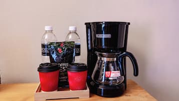 Una cafetera, dos botellas de agua y dos tazas rojas para café sobre una superficie de madera.