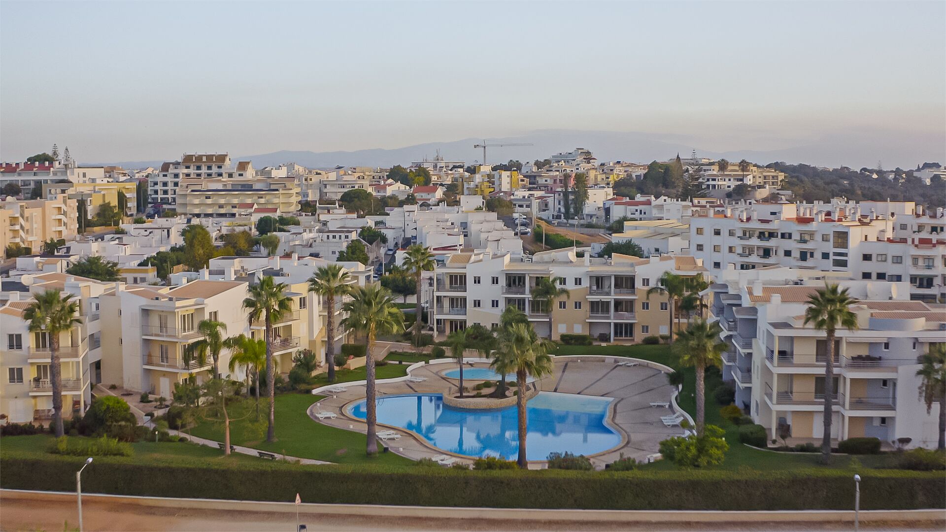 Un quartier résidentiel avec des immeubles d’appartements modernes, une piscine centrale et des palmiers.