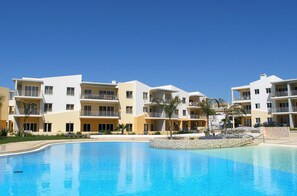 A modern hotel with a swimming pool, multiple balconies, and a clear blue sky. - Portugal Rentals Vila da Praia Apartments (Portimão)