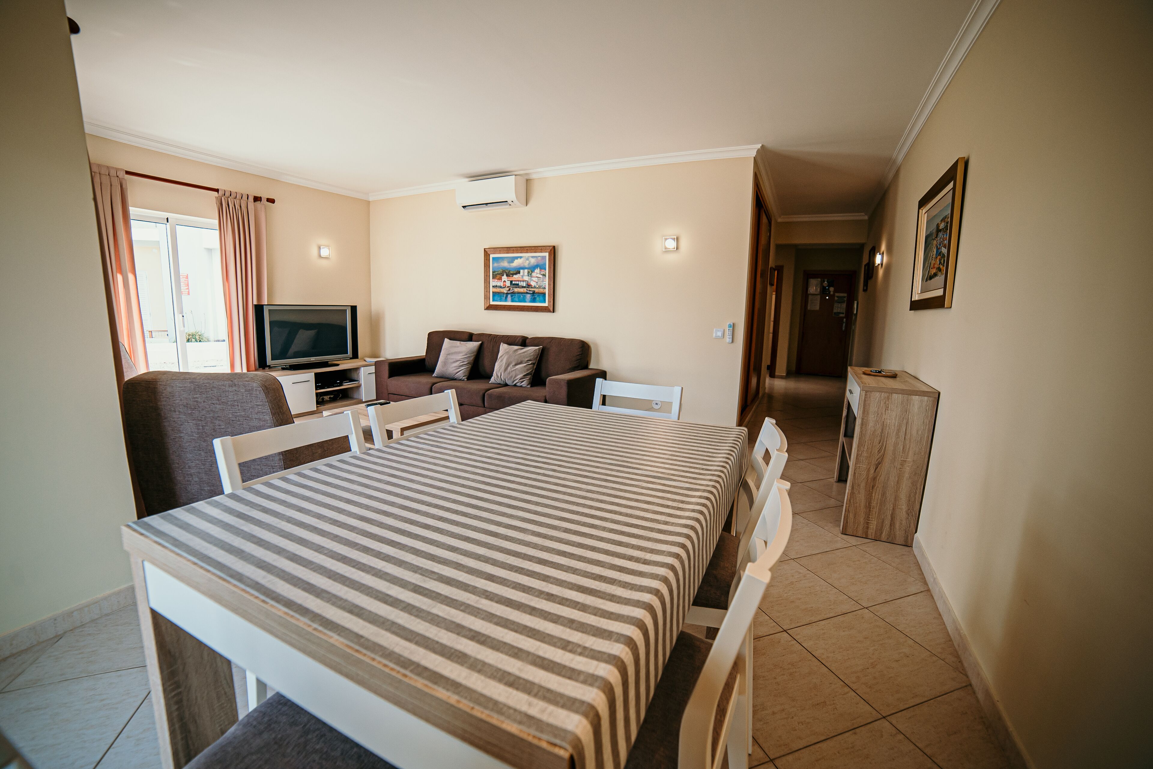 A hotel room with a bed, a TV, a sofa, a dining table, and a small kitchen area.