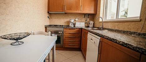 A kitchen with wooden cabinets, a countertop, a sink, a stove, and a dishwasher.