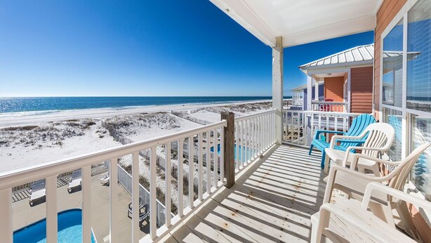 A balcony with a view of the beach, a pool, and a covered area with chairs.