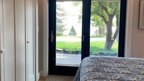 Un dormitorio con cama, una puerta que da a un balcón y vistas a un árbol y un césped.