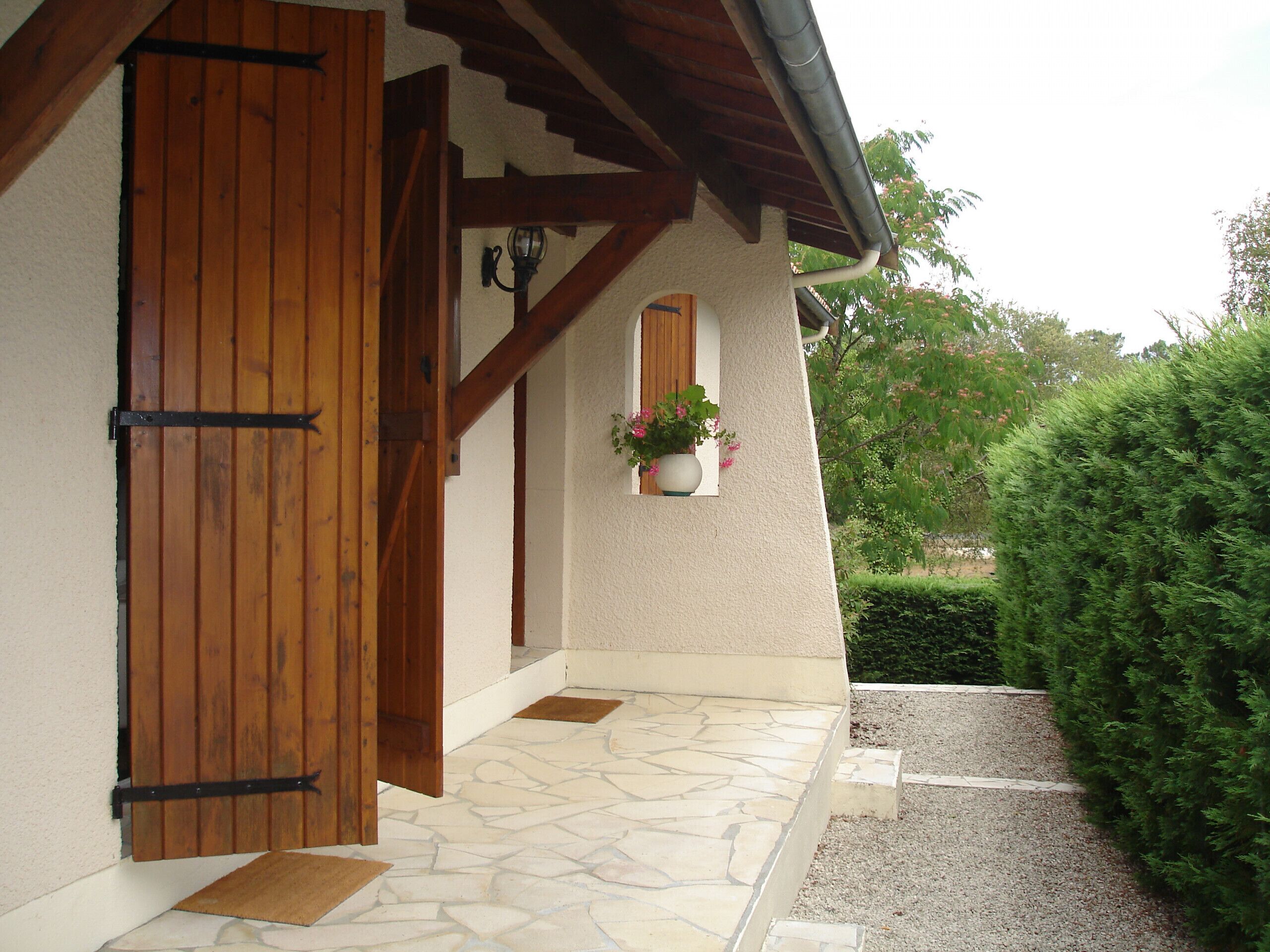 A building entrance with a wooden door, a stone-paved entrance, and a small window with a potted plant.