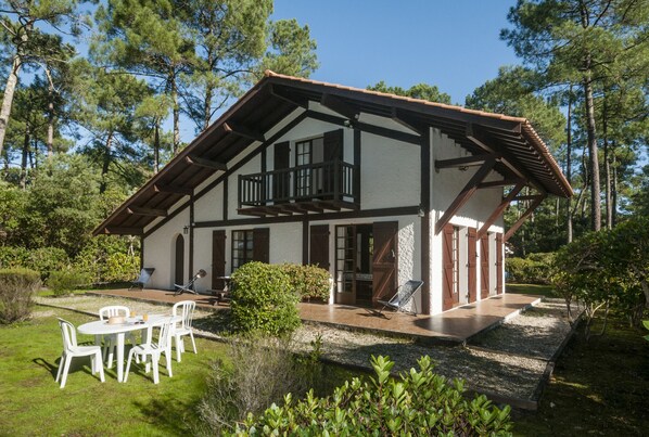 A two-story house with a balcony, a patio with outdoor furniture, and a well-maintained garden.