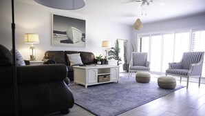 A modern living room with a sofa, a white cabinet, striped chairs, and a large window with blinds.