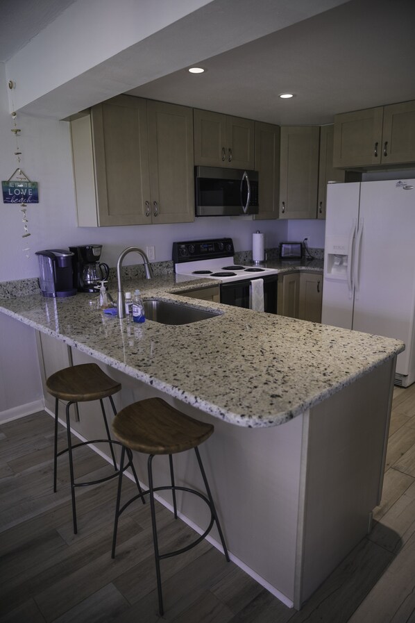 Una cocina con encimeras de granito, electrodomésticos de acero inoxidable y taburetes de madera.