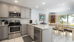 Een moderne keuken met roestvrijstalen apparatuur, een eethoek met houten stoelen, en een groot raam met uitzicht op de omgeving.