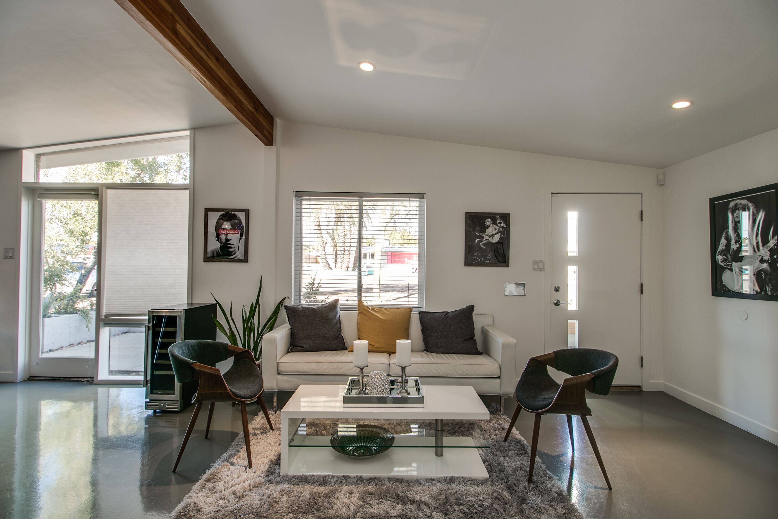 Een moderne woonkamer met een bank, salontafel en stoelen, een salontafel met glazen blad en een groot raam met zonwering.