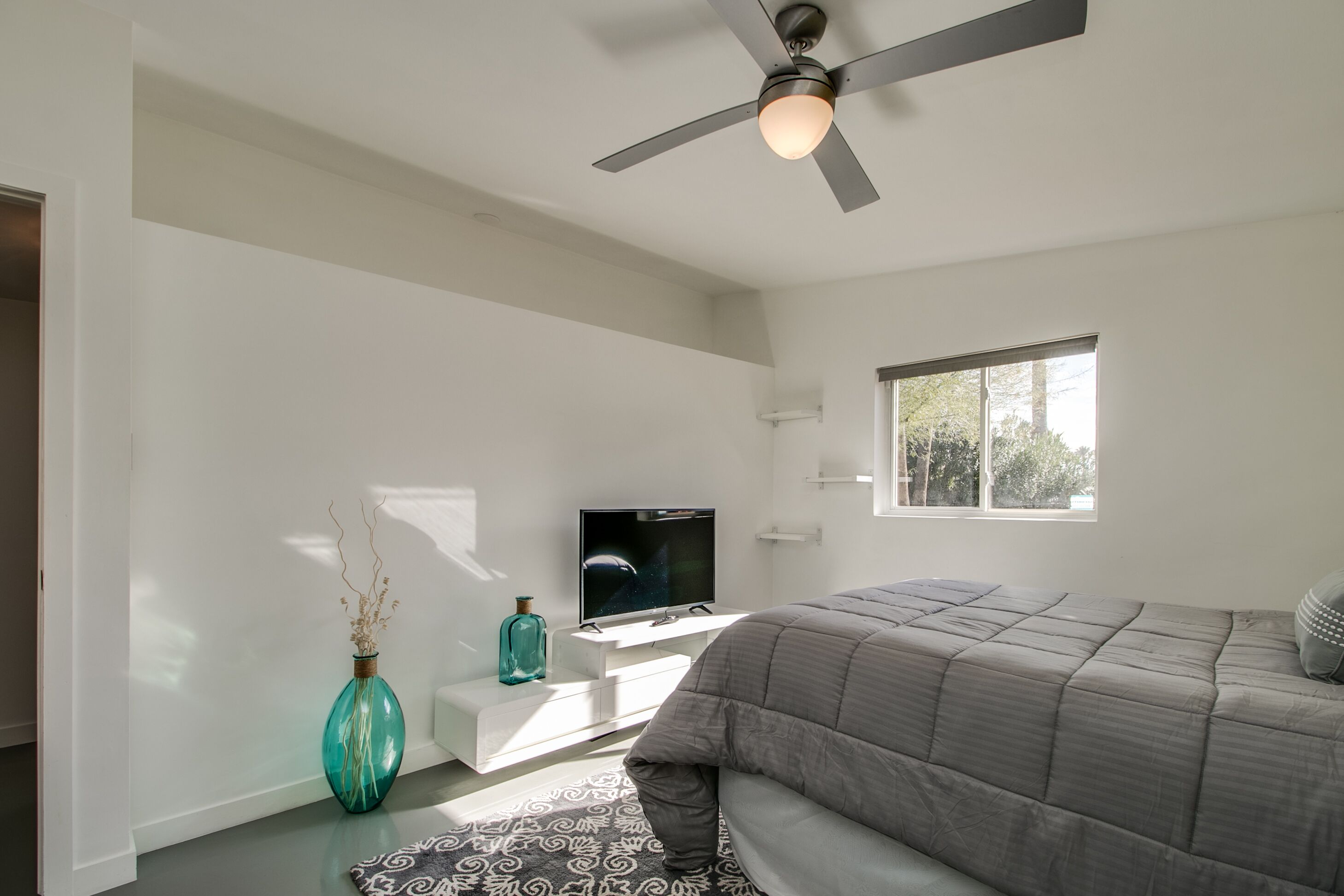 Une chambre à coucher moderne avec un lit, une télévision, un vase et une fenêtre.