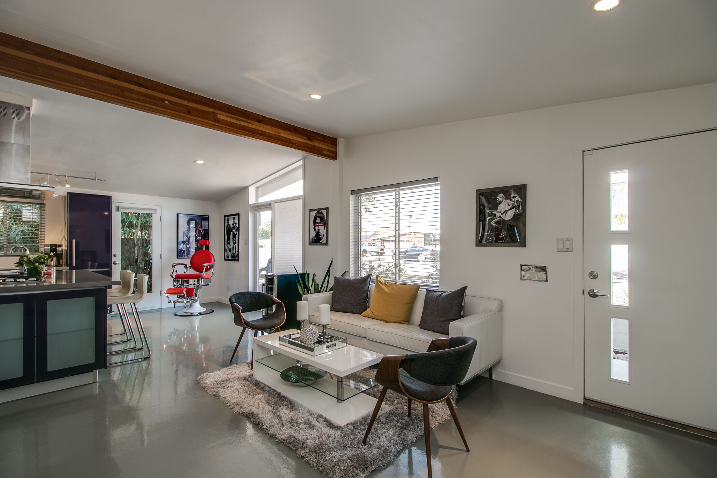 Amplia sala de estar con un sofá blanco, una mesa de centro de cristal y sillas modernas. Hay una zona de cocina con barra y una mesa de comedor.