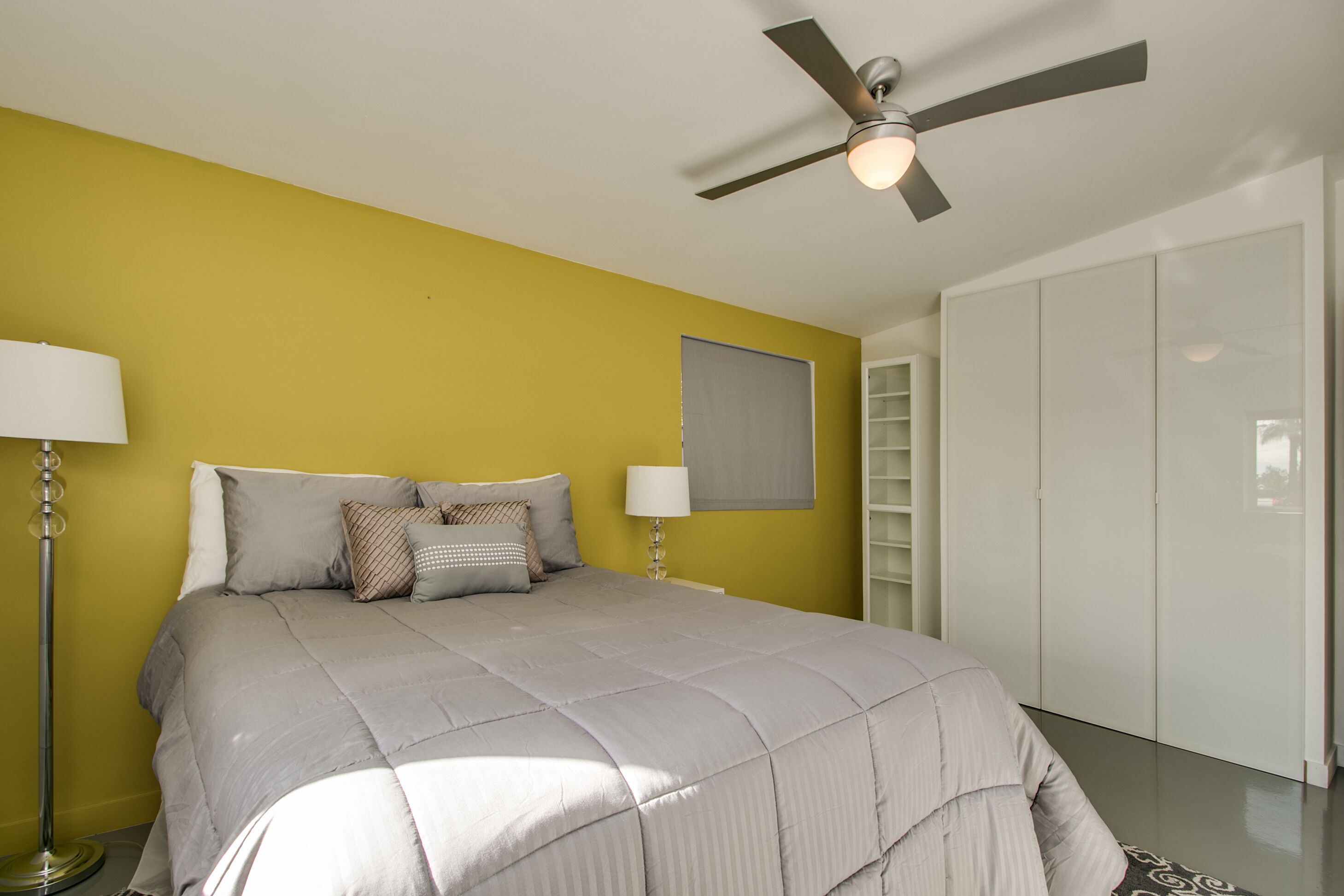 A bedroom with a bed, a ceiling fan, a nightstand, a lamp, and a wardrobe.