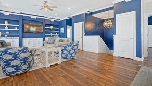 Un salon spacieux doté d’un plancher en bois, d’un ventilateur de plafond, d’une télévision et d’un escalier menant à un autre niveau.