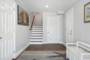 A hallway with white doors, a wooden staircase, and a rug.