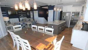 Une cuisine moderne avec des meubles blancs, un grand îlot central et un coin repas comprenant une table en bois et des chaises blanches.