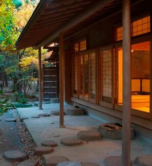 Un edificio japonés tradicional con estructura de madera, escalones de piedra y un jardín de rocas y follaje.