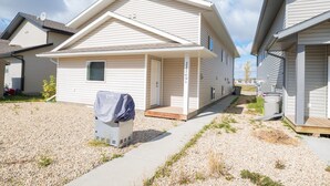 A single-story mobile home with a covered porch, a small attached garage, and a gravel driveway. - Lower Suite Duplex - 3 Beds / 1 Bath By  Restaurants, Costco, G P Airport  (Grande Prairie)