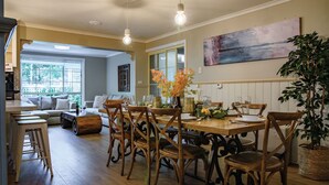A dining area with wooden chairs and a table set for a meal, a sofa, and a large window with a view of greenery. - Frazer Place (Daylesford)