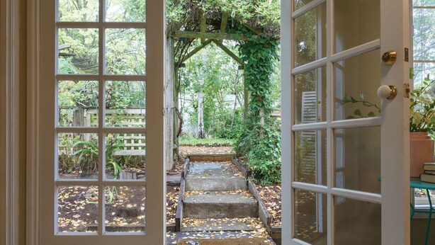 A wooden door with glass panels leading to a garden with a stone staircase and a wooden arbor. - Frazer Place (Daylesford)