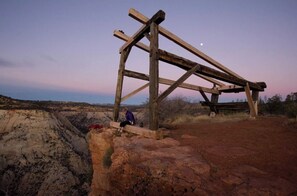 Une structure en bois dans un paysage désertique, avec une personne assise sur un banc.