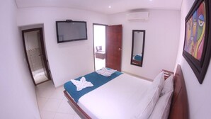 Habitación de hotel con cama, televisión, espejo y puerta que da a un baño.