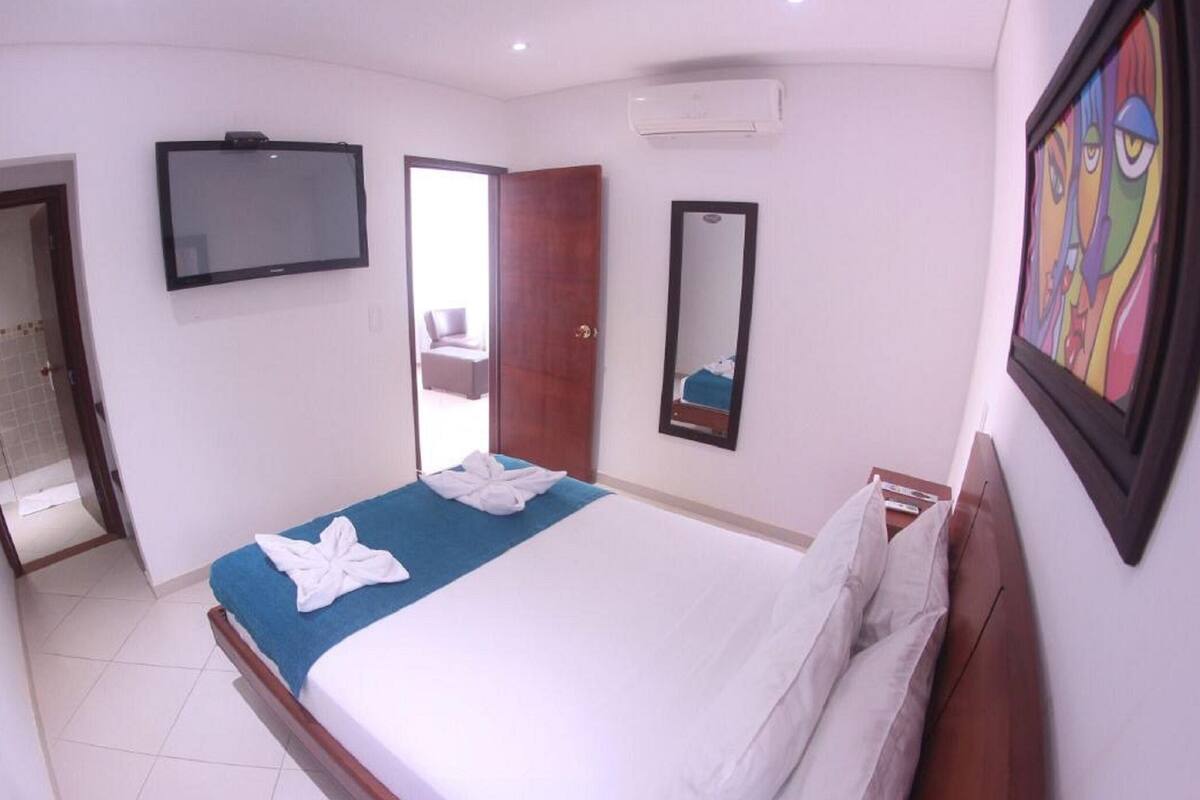 A hotel room with a bed, a TV, a mirror, and a door leading to a bathroom.
