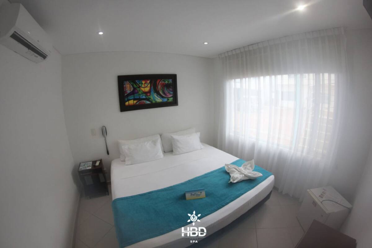 A hotel room with a bed, a painting on the wall, and a window with curtains.