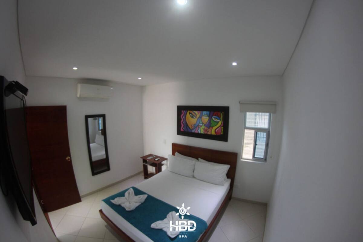 A hotel room with a large bed, a wardrobe, a bedside table, a mirror, and a painting on the wall.