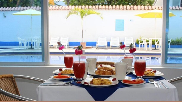 Una mesa de desayuno con platos de comida, bebidas y vistas a una zona de piscina con sillas y sombrillas.