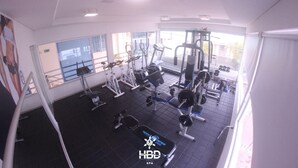 Un gimnasio con diverso equipo de ejercicio, amplias ventanas y vistas al exterior.