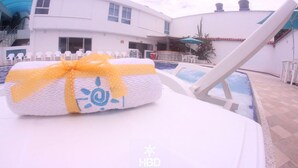 Zona de piscina con una toalla en una silla, un edificio con techo azul y un letrero que dice 'HBD SPA'.