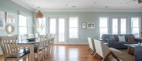 A spacious living room with a dining area, large windows, and a ceiling fan.