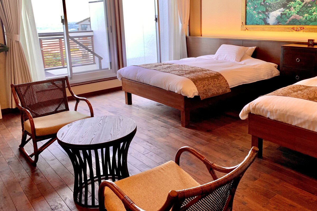 A hotel room with two beds, a small round table, and two wicker chairs.