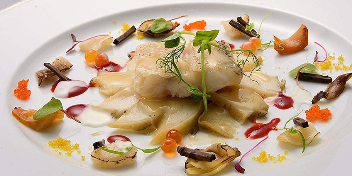 A white plate with a fish dish, garnishes, and small vegetables.