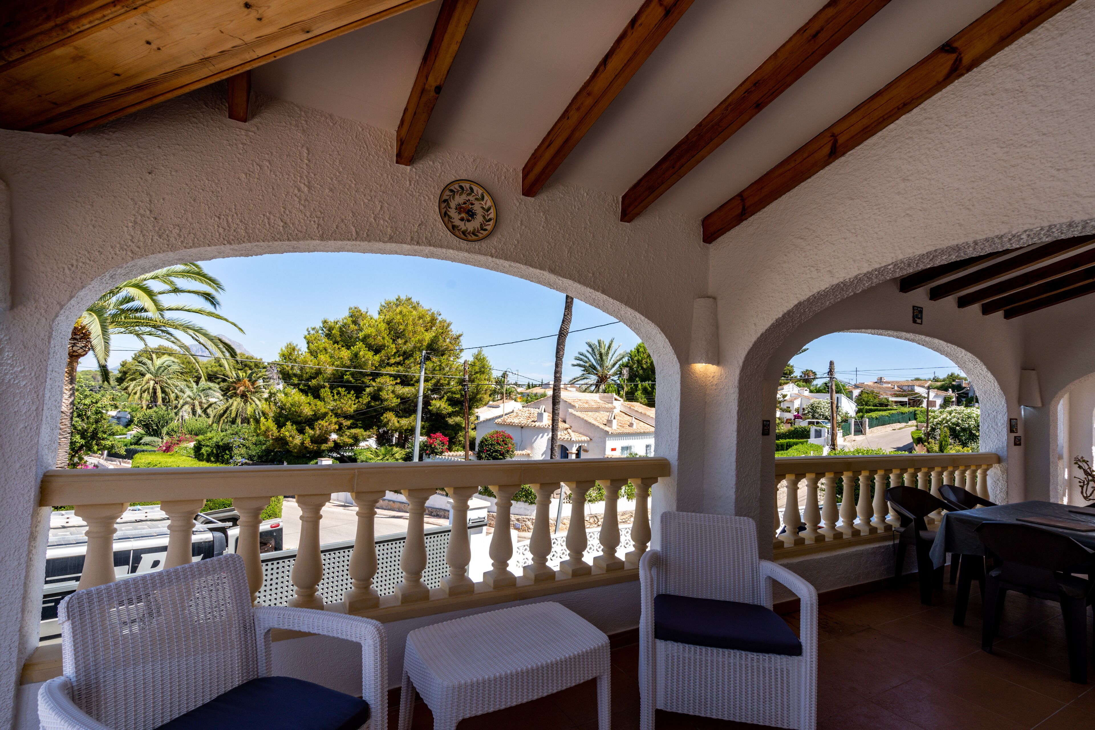 A covered outdoor seating area with white wicker furniture and a view of the neighborhood.