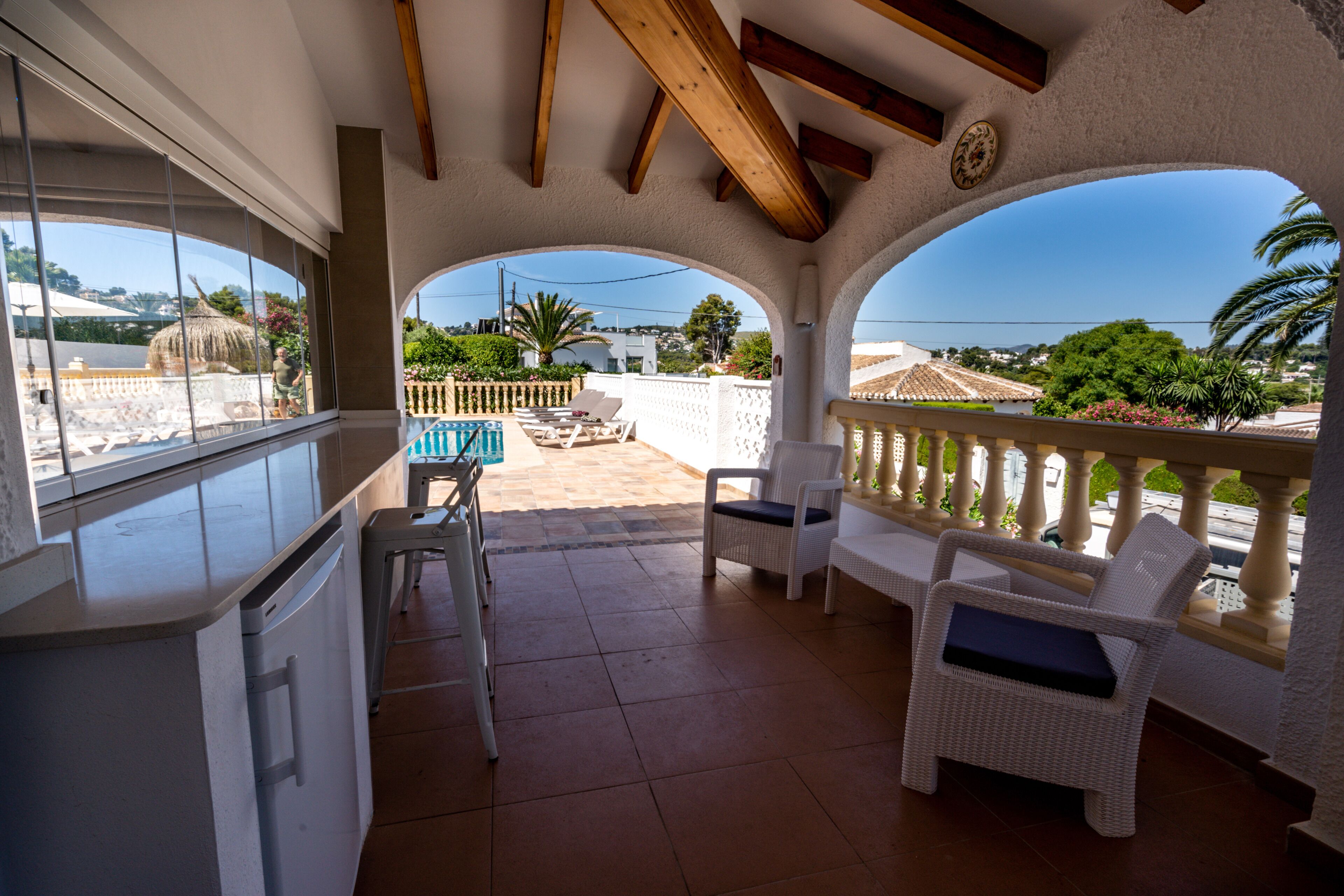 Eine überdachte Terrasse mit weißen Korbmöbeln, einem Pool und Blick auf die umliegende Landschaft.