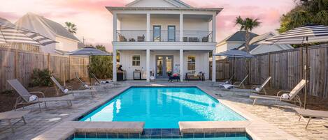 A two-story house with a swimming pool, surrounded by wooden fences and lounge chairs.
