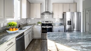 A modern kitchen with white cabinets, stainless steel appliances, a marble countertop, and a central island with a bowl of fruit. - Sleeps 20! 5 Min Walk to Beach, Private Pool & Hot Tub, 8BDR | Lyle by AvantStay (Destin)