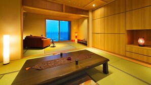 A traditional Japanese room with tatami flooring, a low table with a mat, a sofa, and a sliding door leading to a balcony. - Minshuku Joyama (Himi)