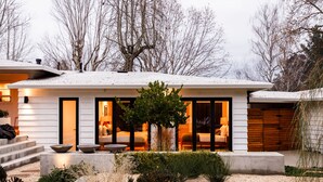 A modern house with a covered patio, large windows, and a well-lit interior.