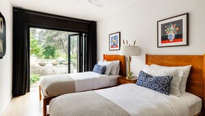 A hotel room with two beds, a ceiling fan, a large window with curtains, and artwork on the walls.